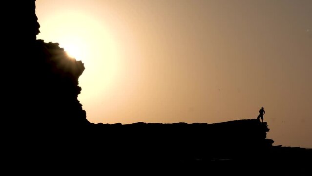 Man with fishing pole at Popoyo Beach Nicaragua over large ocean rocky cliffs during sunset, Handheld silhouette shot