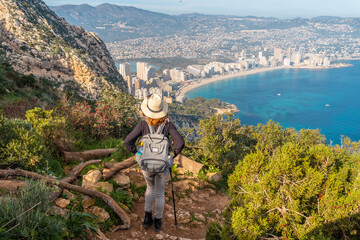 Fototapeta na wymiar A young hiker on the descent path of the Penon de Ifach Natural Park with the city of Calpe in the background, Valencia. Spain. Mediterranean sea. View of La Fossa beach