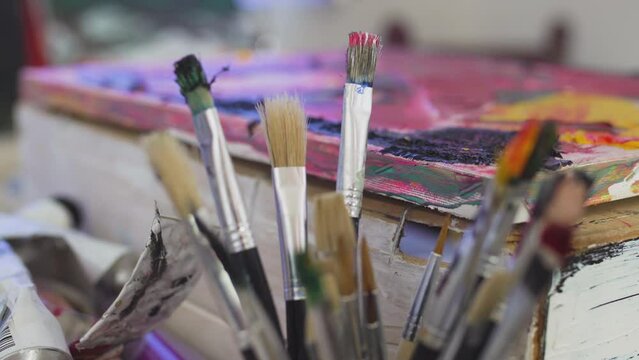 group of abstract used brushes next to an artistic painting. rack focus.
