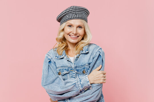 Elderly smiling happy stylish trendy caucasian woman 50s wear denim jacket hat beret hold hands crossed folded isolated on plain pastel light pink background studio. People lifestyle fashion concept
