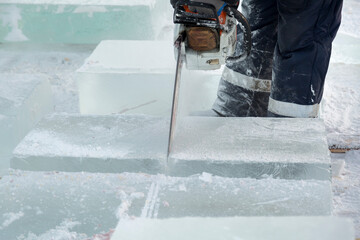 Worker cuts a lump of ice with a chainsaw