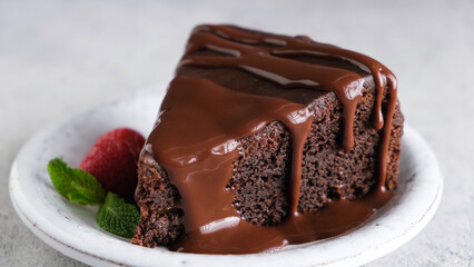 Slice of chocolate brownie cake with chocolate glaze on top served on dessert plate, closeup view. Rich in sugar and fats dessert