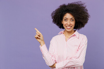 Young fun woman of African American ethnicity 20s in pink striped shirt point index finger aside on workspace area mock up copy space isolated on plain pastel light purple background studio portrait