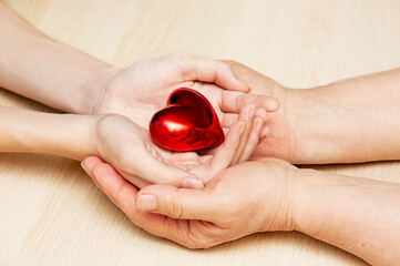 Adult and child hands holding a heart on a wooden background