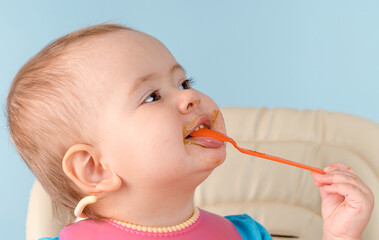 A happy smiling baby 12-17 months old eats broccoli vegetable puree with a spoon