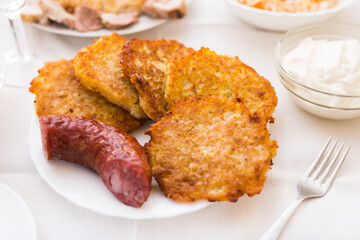 Potato pancakes with fried sausage on white plate