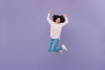 Full size overjoyed excited happy young woman of African American ethnicity 20s wear pink striped shirt jump high clench fist say yes isolated on plain pastel light purple background studio portrait.