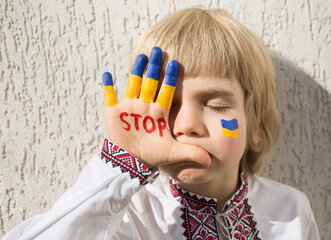 face of boy in national Ukrainian clothes, inscription STOP on his hand, fingers are painted in...
