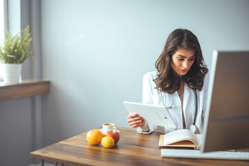 Smiling female nutritionist in her office, writing diet plan showing healthy vegetables and fruits....
