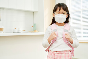Elementary school Korean girl wearing a mask with a backpack in front of the kitchen