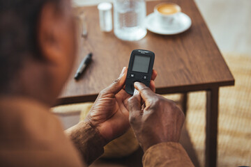 Medicine, age, diabetes, health care and old people concept - senior African man with glucometer checking blood sugar level at home. Measuring blood glucose with glucometer closeup.
