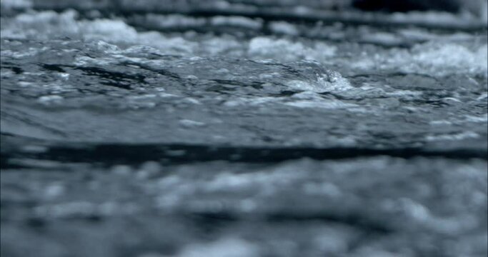 Close-up of water flowing by in slow motion on a river from the side with depth of field,