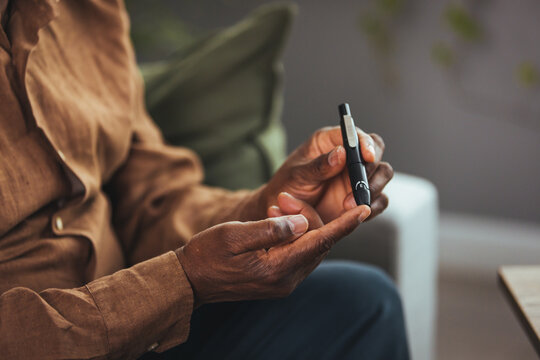 Senior man with glucometer checking blood sugar level at home. Elderly man testing for high blood sugar. Man holding device for measuring blood sugar