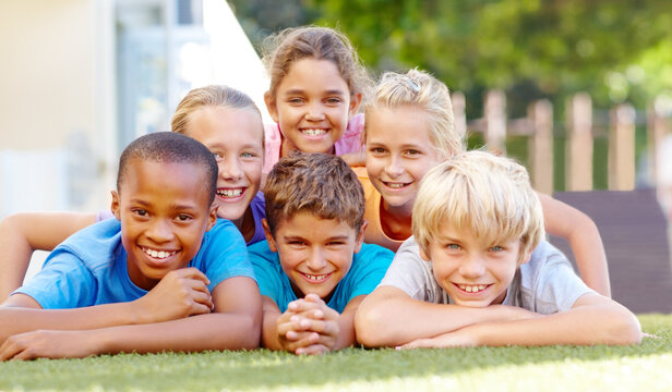 Healthy lifestyles make happy kids. A group of cute primary school kids lying down in pyramid formation outside. - Powered by Adobe