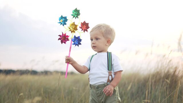 kid walk pinwheel. little baby boy play with windmill toy wind in the park. happy family kid dream concept. baby boy play toy sunset pinwheel sun walk the glare of at fun in the park