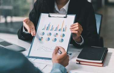 Business man holding a pen and analysis documents on office table with laptop computer and graph financial diagram working in the background.