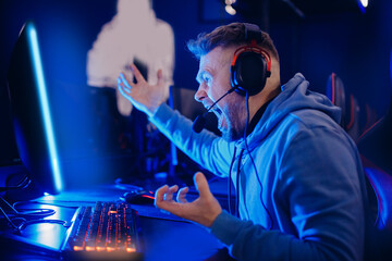 Streamer young man angry professional gamer playing online losing game computer with headphones, neon color © Parilov