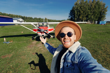 Concept travel trip private aviation. Selfie photo happy tourist man pilot in hat and glasses background white aircraft cockpit