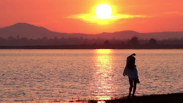 Happy woman dancing beside the lake  with sunrise background