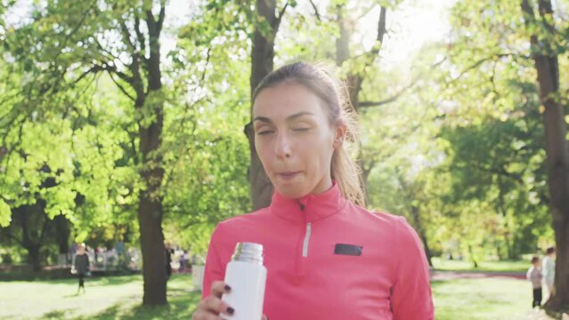 Fitness girl in pink sportswear drinking water from a bidon in the park