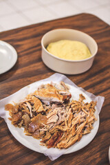 Pork carnitas on a plate accompanied with yellow corn tortillas out of focus in the background on a wooden table. Traditional Mexican food.