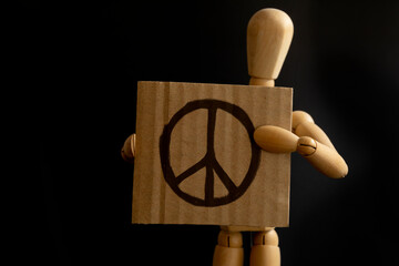 Wooden doll holding peace symbol on black background, for peace on Ukraine