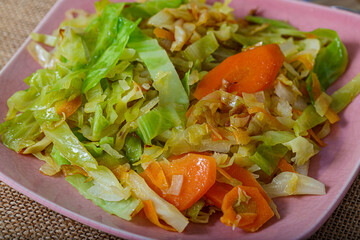 Cabbage fried or stewed with herbs, carrots, onions on a pink square plate. Soft focus. Vegetarian healthy tasty food.