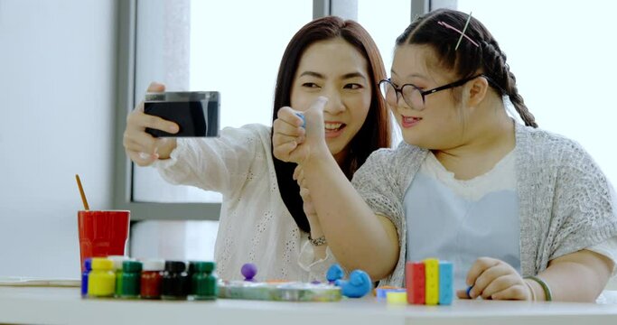 Asian mother and Autistic daughter learning to practice Plasticine and painting Study online via smartphone at home with intention happy. Girl enjoy doing art activities to enhance imagination skill