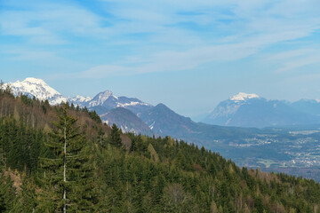 Scenic view of snow capped mountain peaks of Karawanks near Sinacher Gupf in Carinthia, Austria. Mount Mittagskogel and Dobratsch is visible through dense forest in early spring. Sunny Rosental