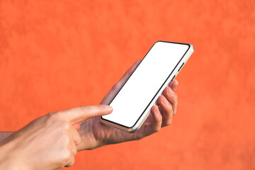 Finger in front of a mockup of a smartphone in a girl's hand. Against the background of an orange facade made of decorative plaster. Close-up.