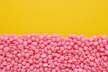Beautiful pink depilatory wax granules on a yellow background. Epilation, depilation, unwanted hair removal. Top view. Place for text.