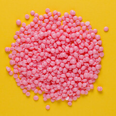 Beautiful pink depilatory wax granules on a yellow background. Epilation, depilation, unwanted hair removal. Top view.