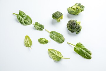 spinach leaves and broccoli slices lie on a white uniform background