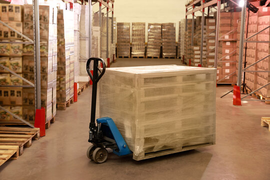 Modern manual forklift with wrapped wooden pallets in warehouse