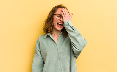 young pretty woman laughing and slapping forehead like saying d’oh! I forgot or that was a stupid...