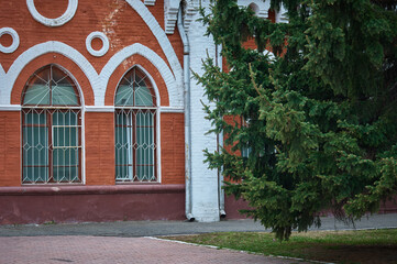 Fototapeta na wymiar The facade of a historical building made of red brick in the pseudo-Gothic style of architecture. Fluffy branches of an evergreen spruce. Former malls. 