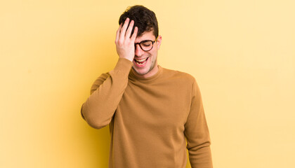 young handsome man laughing and slapping forehead like saying d’oh! I forgot or that was a stupid...