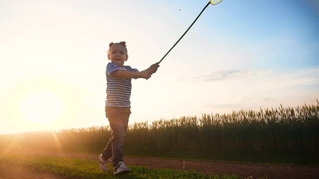 little girl with a butterfly net. a child runs with a butterfly net in the park through a nature field in summer catches insects. happy family kid dream concept. fun baby play in the summer run