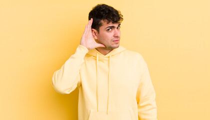 young handsome man looking serious and curious, listening, trying to hear a secret conversation or...