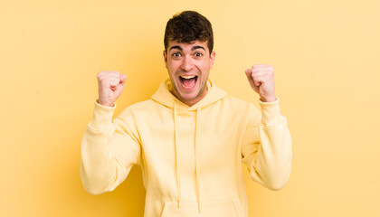young handsome man feeling happy, positive and successful, celebrating victory, achievements or...