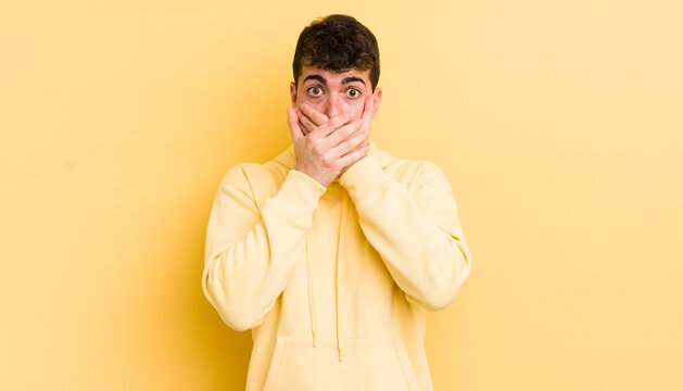 young handsome man covering mouth with hands with a shocked, surprised expression, keeping a secret or saying oops