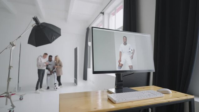 Monitor with an advertising cover of the picture On the background a photographer, a football player, a model and a director look at photos from a photo shoot for the cover on a camera