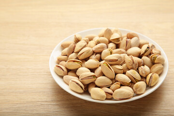 Pile of Pistachios ob white bowl on grey wooden background.