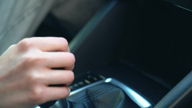 A hand of driver woman is shifting the manual gear in a car close up view. Girl controls auto and switch speed on gearbox, turn on. Unrecognizable female red nails driving and changing gear.