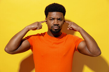 Fototapeta na wymiar Young man of African American ethnicity 20s wear orange t-shirt cover ears with hands fingers do not want to listen scream isolated on plain yellow background studio portrait People lifestyle concept