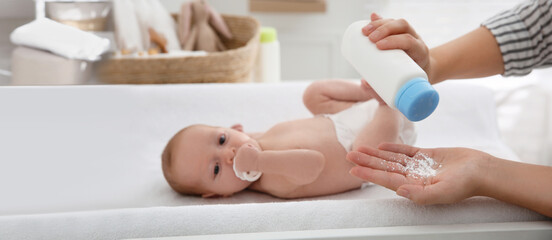 Mother with bottle of dusting powder near her cute baby at home. Banner design