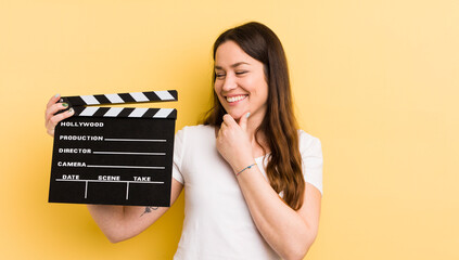 young pretty woman smiling with a happy, confident expression with hand on chin. cinema clapper...