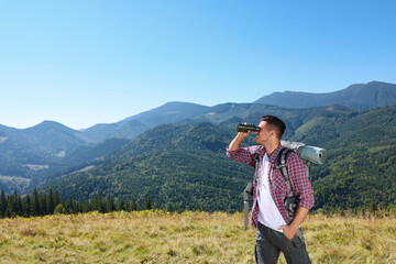 Tourist with hiking equipment looking through binoculars in mountains