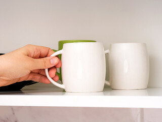 A woman taking a white mug from a shelf
