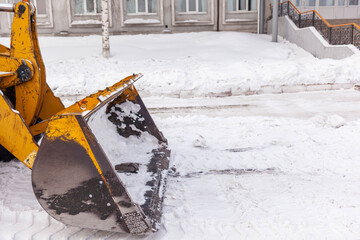 Big orange tractor cleans up snow from the road and loads it into the truck. Cleaning and cleaning of roads in the city from snow in winter. Snow removal after snowfall and blizzards. 